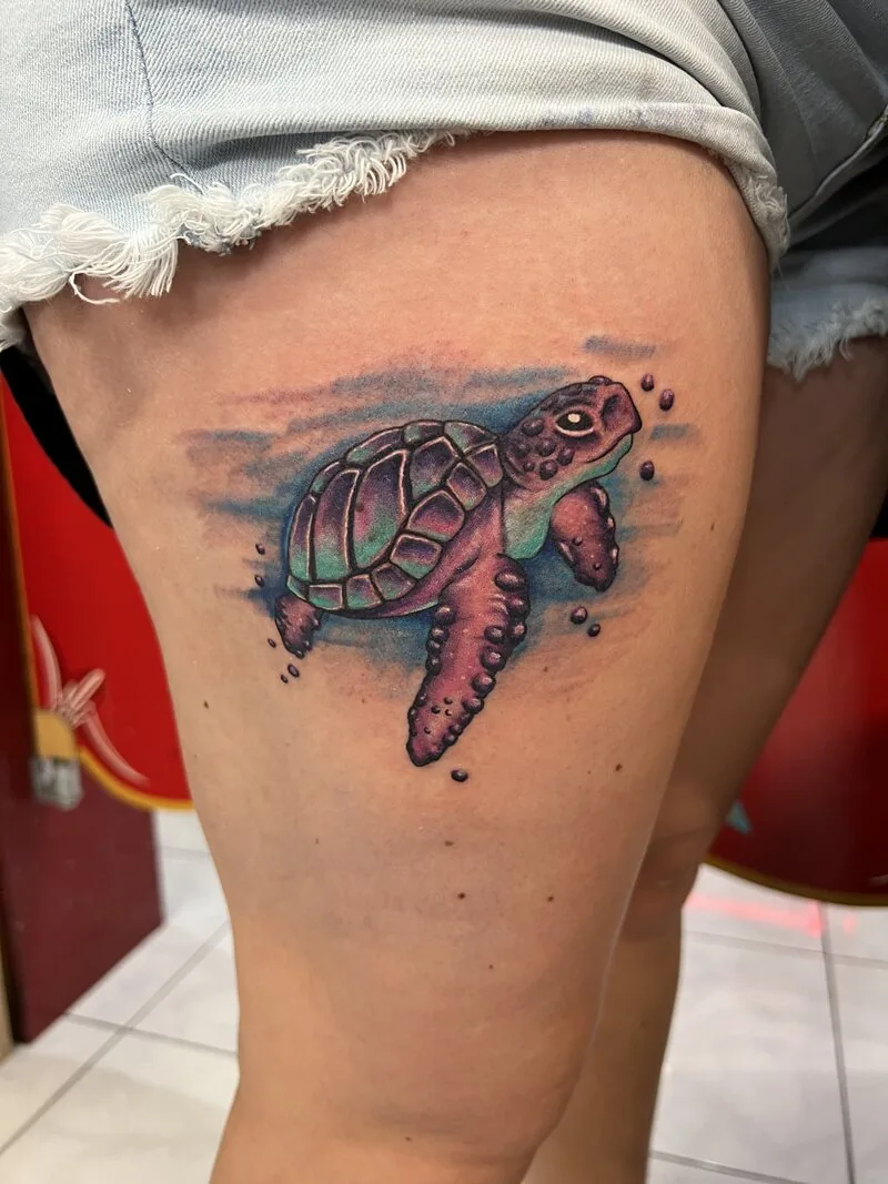 Watercolor-style sea turtle tattoo on the thigh, rendered in soft pinks and teals with painted splash backdrop, by Dustin Gormley at Ohana Tattoo, Waikiki, Hawaii.