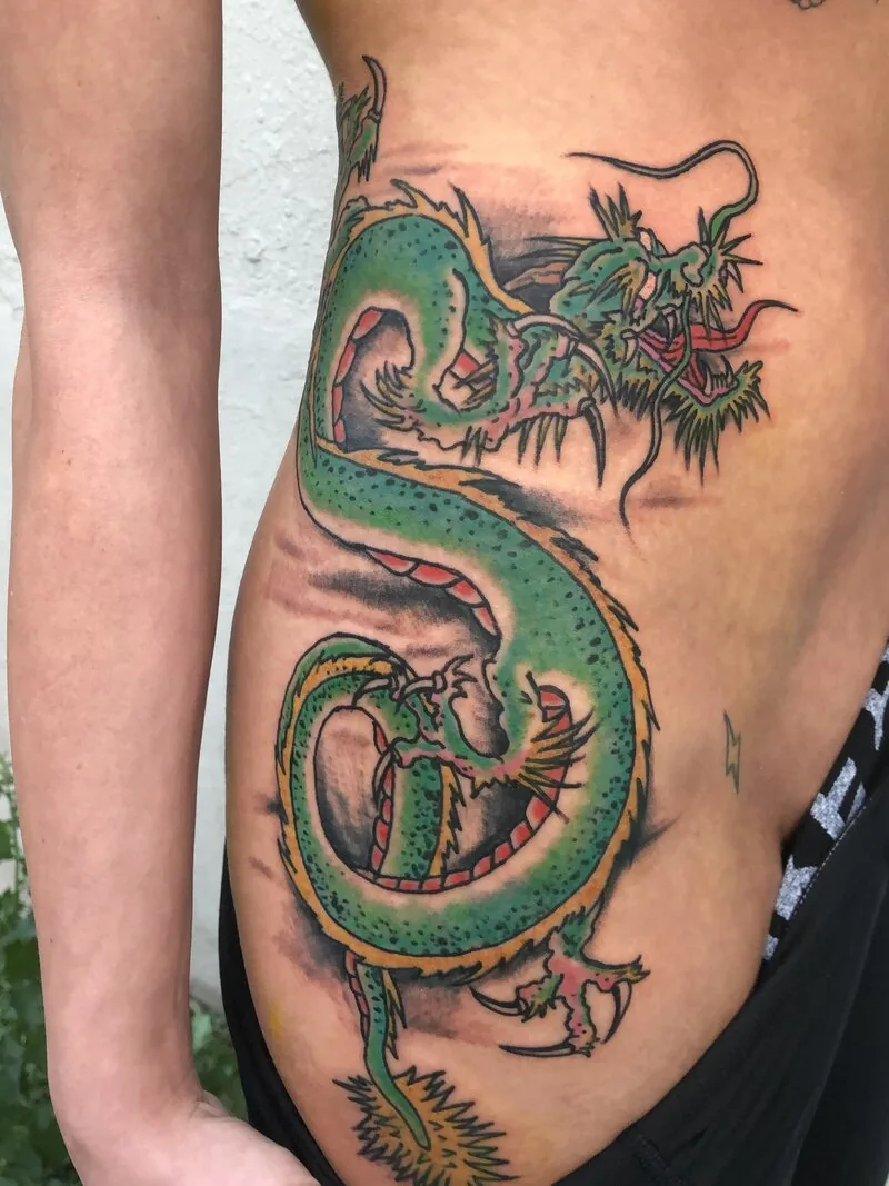Asian Traditional dragon tattoo coiling down the ribs in green with red dorsal scales and yellow claws, by Dustin Gormley at Ohana Tattoo, Waikiki, Hawaii.