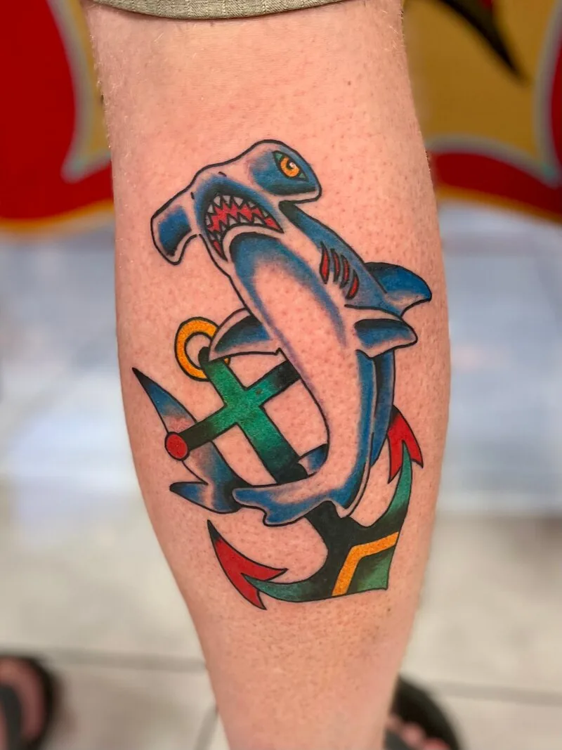 American Traditional color tattoo of a hammerhead shark swimming through a green anchor with red accents, on a calf, by Dustin Gormley at Ohana Tattoo, Waikiki, Hawaii.