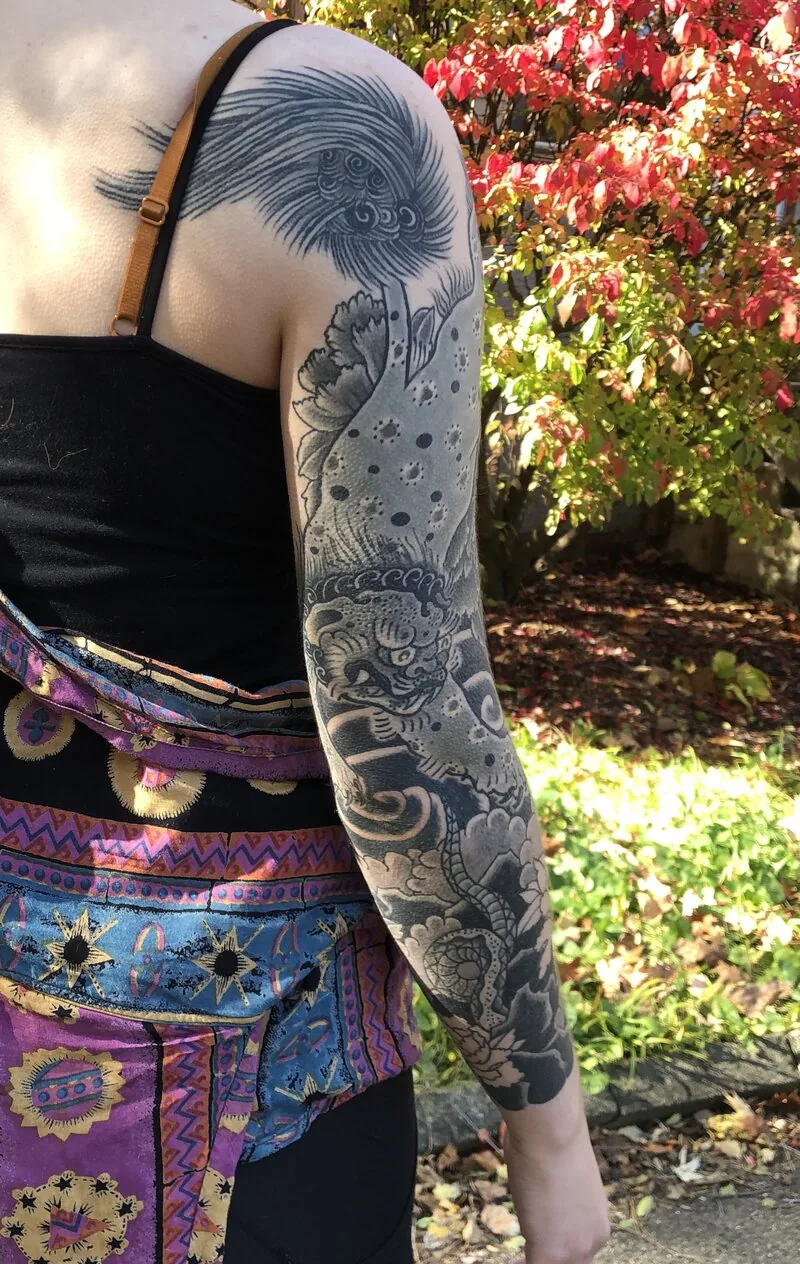 Black and grey Japanese full sleeve tattoo with foo dog, peonies and wind bars, by Dustin Gormley at Ohana Tattoo, Waikiki, Hawaii.
