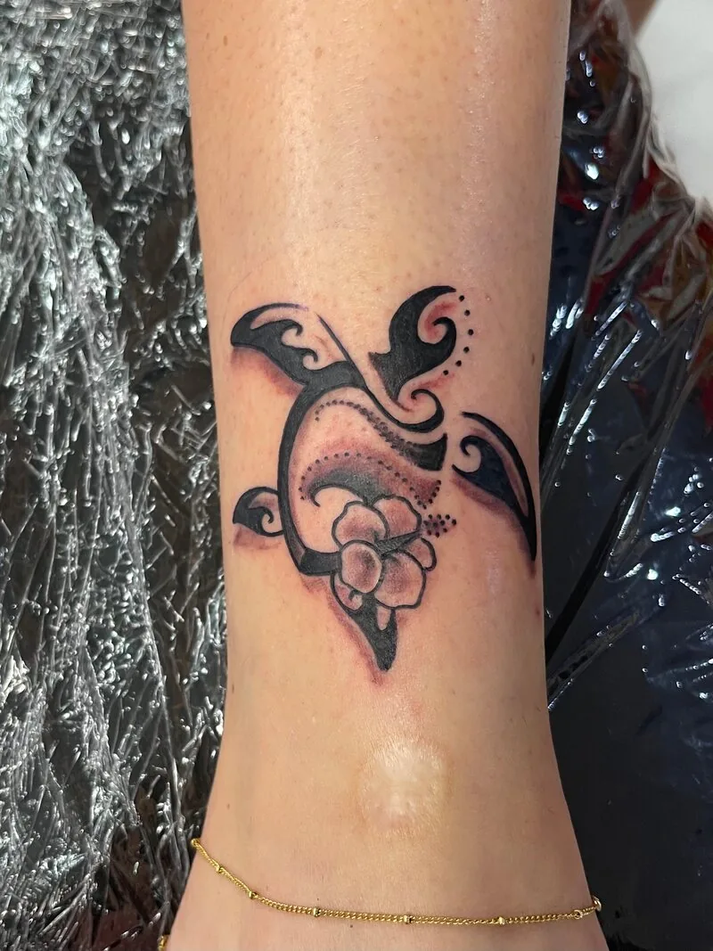 Polynesian tribal silhouette tattoo of a honu sea turtle with a small plumeria flower inside its body, on an ankle, by Dustin Gormley at Ohana Tattoo, Waikiki, Hawaii.