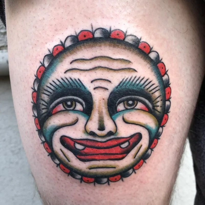 Small American Traditional flash tattoo of a smiling moon face with red dot border on the thigh, by Dustin Gormley at Ohana Tattoo, Waikiki, Hawaii.